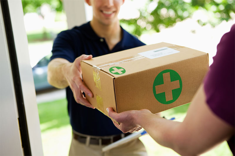 Delivery person handing a package with a green medical cross symbol to a customer at the door