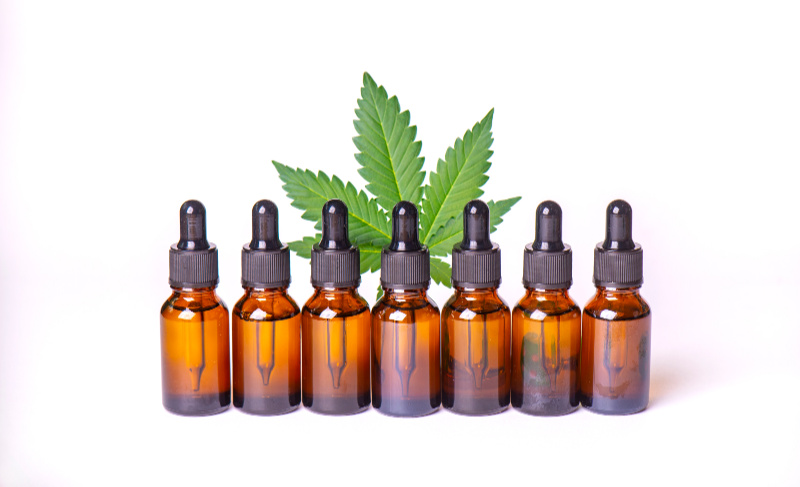 Row of amber dropper bottles displayed in front of a green cannabis leaf on a white background.