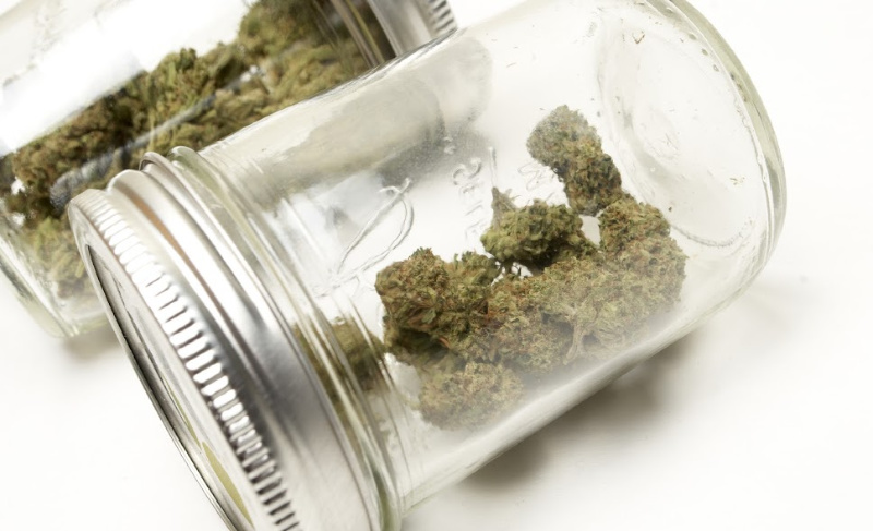 Glass jar tipped on its side containing cannabis flower buds against a white background.