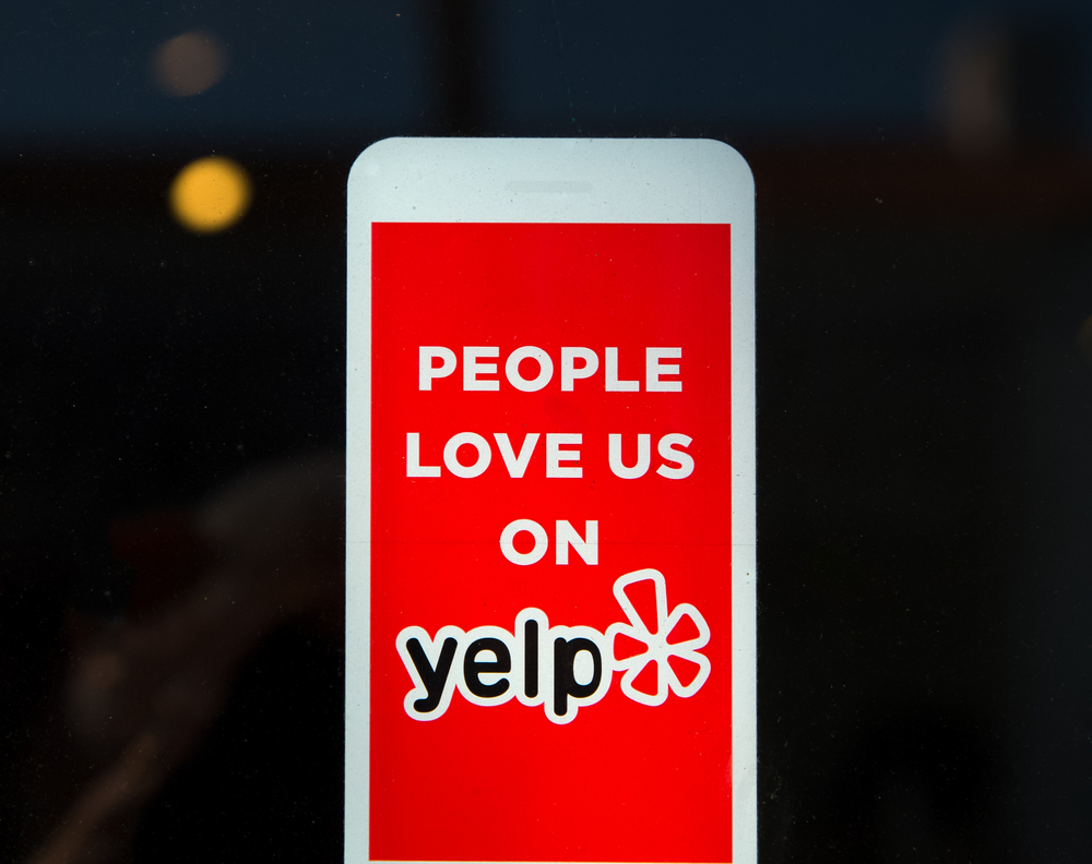 Red sign reading People love us on Yelp with the Yelp logo displayed on a glass surface.