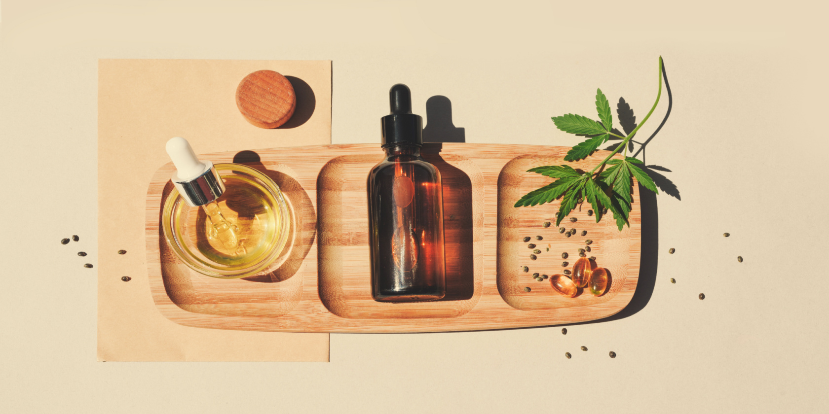 Top-down view of cannabis wellness products, including oil droppers, amber bottles, capsules, and a cannabis leaf arranged on a wooden tray.