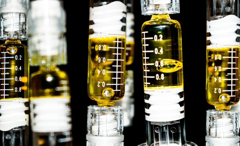 Close-up of laboratory glass syringes filled with golden cannabis oil, showing measurement markings against a dark background.